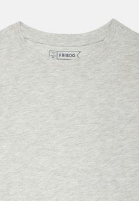 Világosszürke, kerek nyakú póló puha, texturált anyagból. A nyakkivágásnál egy címke található, amelyen a márkanév és a méretadatok szerepelnek.