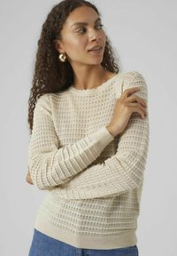 Maglione lavorato a maglia beige con un motivo testurizzato, dotato di maniche lunghe e scollo a costine, che presenta un design a tessitura aperta.