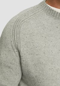 Hellgrauer Pullover aus strukturiertem Strick, mit rundem Ausschnitt und dezenten gesprenkelten Mustern. Verstärkte Schulternähte sind sichtbar.