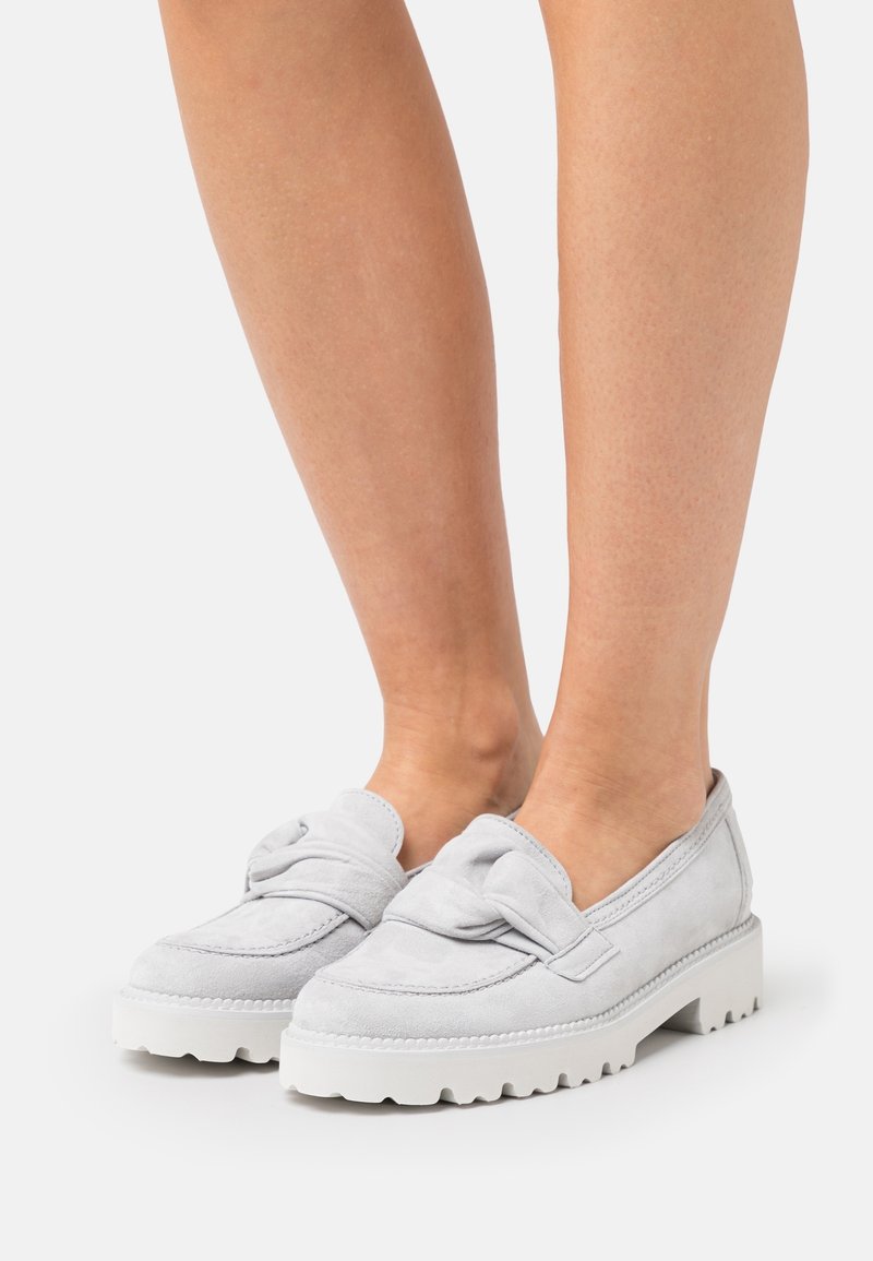 Mocassins en daim gris clair avec un détail de nœud, semelle épaisse en caoutchouc blanc et accents de couture. Design à coupe basse révélant la cheville.
