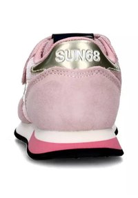 Růžové semišové tenisky s metalickým zlatým detailem na patě, bílou mezipodešví a černou podrážkou. Na zadní části mají výrazné logo.