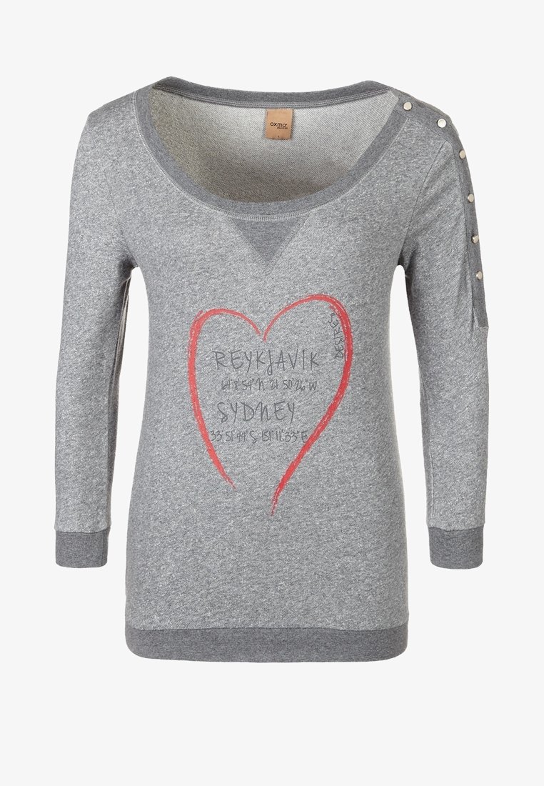 Chemise grise à manches longues avec détail bouton à l’épaule, motif cœur rouge, et texte « Reykjavik » et « Sydney » avec coordonnées au centre.