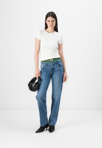 Hvit tettsittende t-skjorte kombinert med høytlivs blå jeans med grønt mønstrete liv. Svart håndveske og spiss tå hæler.