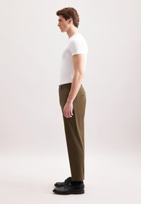 T-shirt bianca a maniche corte abbinata a pantaloni verdi oliva, dal taglio aderente e con tasche laterali visibili, indossati con scarpe nere.