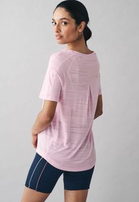 Lyserød trænings T-shirt med struktureret overflade, korte ærmer og slids bagpå, parret med marineblå cykeltights med hvide og lyserøde detaljer.