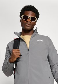 Pilkas zip-up džemperis su geometrine tekstūra ir The North Face logotipu ant kairio peties. Derinamas su šviesiais akinių nuo saulės.