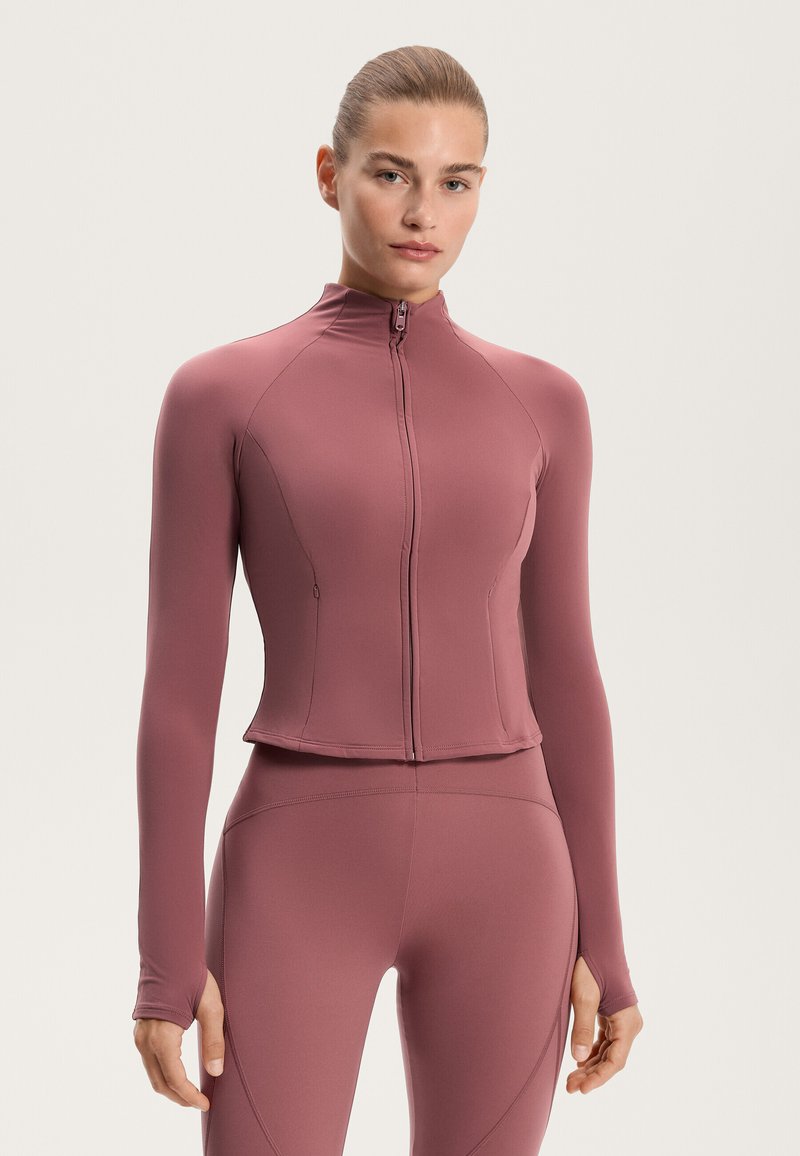 Long-sleeve fitted jacket in soft mauve fabric, high collar, front zipper, and thumbholes at cuffs, paired with matching fitted leggings.