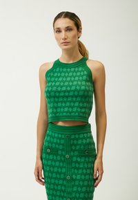 Top corto de punto verde con patrón geométrico, combinado con una falda a juego que presenta botones y bolsillos. Ambos artículos muestran un acabado texturizado.