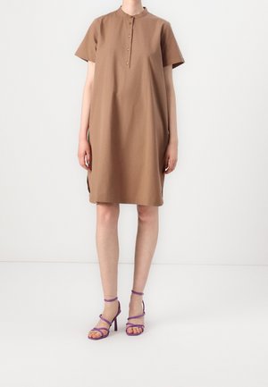 Woman wearing a knee-length, short-sleeve brown dress with a buttoned collar and purple high-heeled strappy sandals.