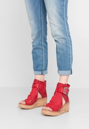 Punaiset nahka wedgesandaalit, joissa on avonainen varvas, nilkkaremmillä ja soljella. Yhdistetty kääntövarrella vaaleansinisiin farkkuihin.