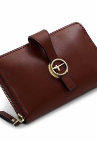 Brown leather wallet with a smooth texture, rounded shape, and a gold circular hardware accent. Features a zip closure and strap.