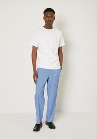 Camiseta blanca de manga corta combinada con pantalones claros a rayas, que presentan un corte relajado y zapatos de vestir negros. Diseño simple y colores monocromáticos.