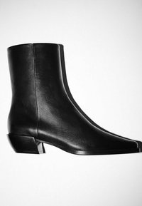 Bottine en cuir noir à cheville avec talon bloc bas, surface lisse et détail de couture latérale sur fond blanc.