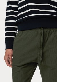 Felpa a righe blu navy e bianca con polsini a coste abbinata a pantaloni con cordoncino in tessuto verde oliva, che mostrano una vestibilità rilassata e dettagli.