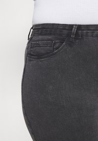 Los vaqueros de mezclilla negra presentan un diseño ajustado con una cintura de altura media, costuras sutiles y un estilo clásico de cinco bolsillos. La textura parece suave.