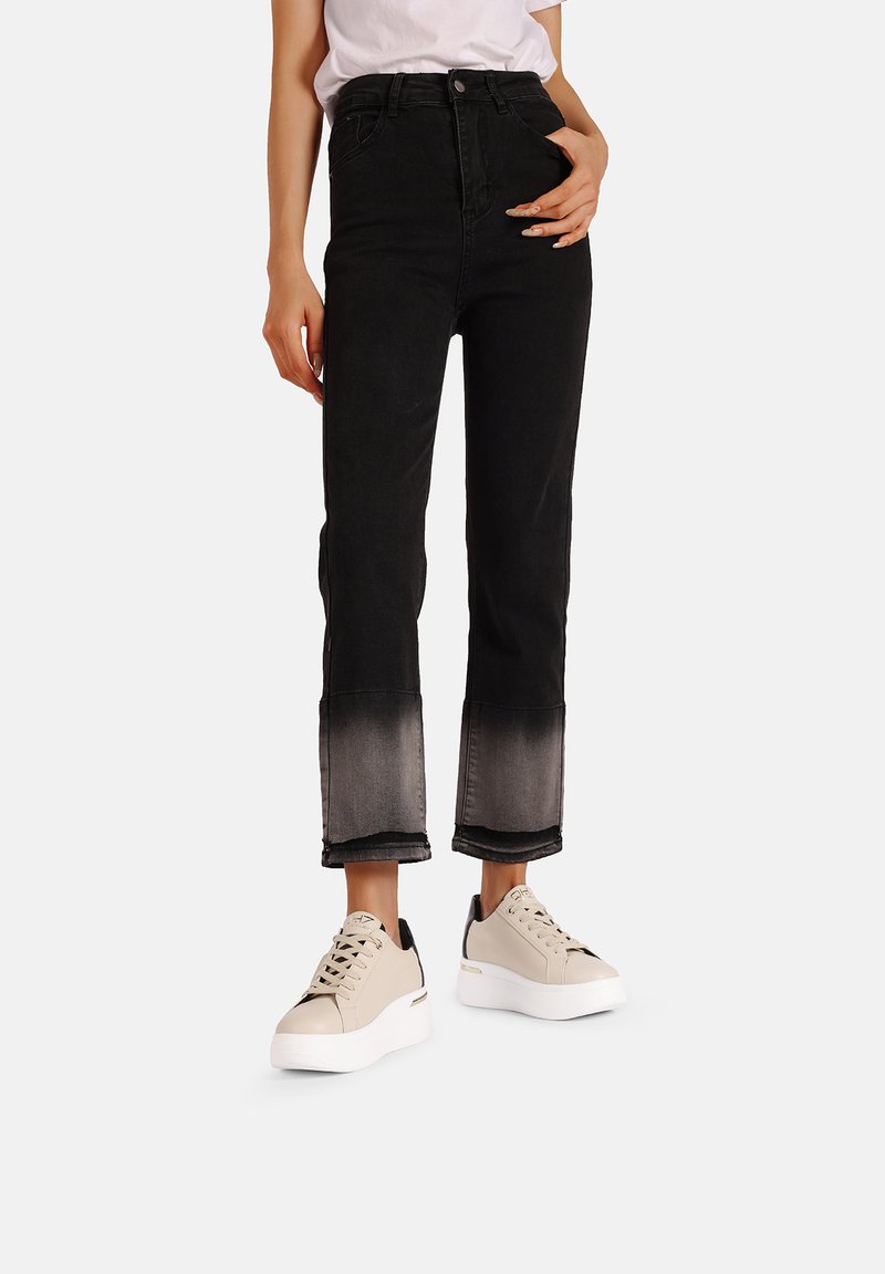 Jeans neri a vita alta con una graduale sfumatura al grigio all'orlo, abbinati a sneakers beige con una suola bianca spessa.