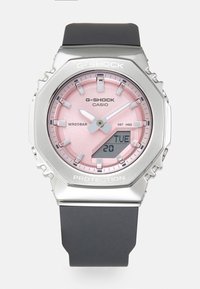 Montre G-SHOCK avec un boîtier en acier inoxydable argenté, un cadran rose, un bracelet en caoutchouc noir, un affichage analogique et numérique, et une résistance à l'eau jusqu'à 20 bars.