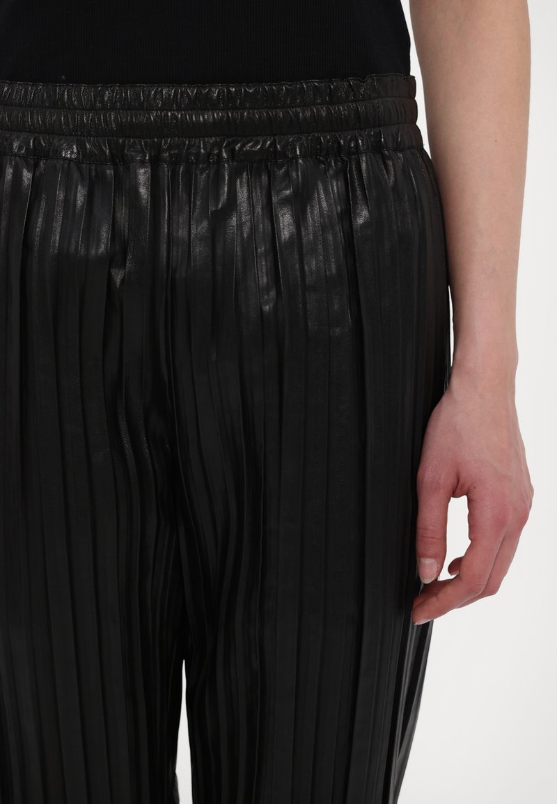 Svarta veckade byxor i glänsande material med elastisk midja, med smala, vertikala veck och en slät yta.