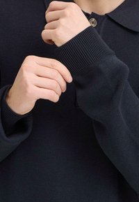 Marineblauer Strickpullover mit Kragen, ausgestattet mit Knopfschluss und gerippten Bündchen. Das Material wirkt weich und hat eine strukturierte Oberfläche.