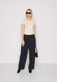 Μπεζ κοντομάνικο μπλουζάκι με εκτύπωση λογοτύπου, ψηλόμεσο ναυτικό παντελόνι με φαρδιά πόδια, μαύρη τσάντα χεριού και μαύρες κομψές μπότες με μυτερή μύτη και λεία υφή.