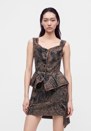 Frau mit langen dunklen Haaren, die ein dunkel gemustertes ärmelloses, geknöpftes Oberteil mit Peplum und einem passenden asymmetrischen Rock trägt.