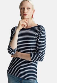 Granatowa i biała w paski bluzka z długim rękawem i dekoltem w łódkę, wykonana z miękkiej bawełny i dopasowana do sylwetki, w połączeniu z jasnoniebieskimi dżinsami.