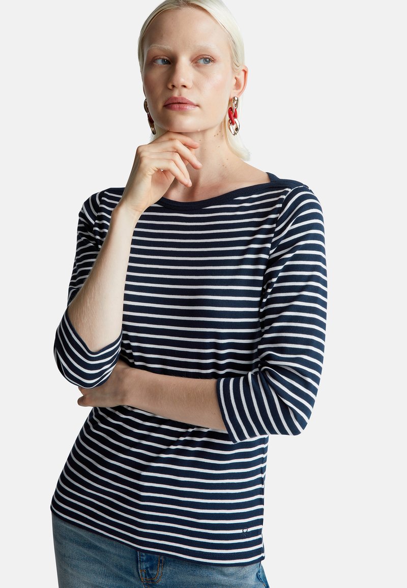 Granatowa i biała w paski bluzka z długim rękawem i dekoltem w łódkę, wykonana z miękkiej bawełny i dopasowana do sylwetki, w połączeniu z jasnoniebieskimi dżinsami.