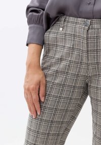 Pantaloni a quadri in grigio chiaro e beige, realizzati in un tessuto testurizzato. Presentano una vestibilità slim, bottone in vita e un piccolo logo metallico decorativo.