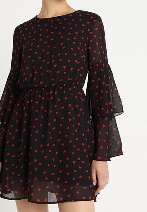 Schwarzes Kleid mit rotem Herzmuster, durchsichtige Glockenärmel und taillierte Taille, getragen von einer Person, die vom Hals bis zur Mitte des Oberschenkels gezeigt wird.