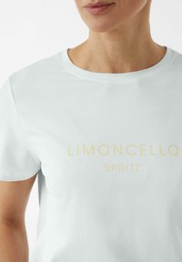 Jasnoniebieska koszulka z okrągłym dekoltem i krótkimi rękawami. Z przodu znajduje się napis "LIMONCELLO SPRITZ" w żółtej, prostej czcionce. Miękka tekstura.