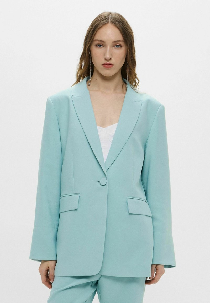 Blazer verde menta con un design strutturato, chiusura a un bottone, rever con allacciatura e tasche laterali. Tessuto liscio con una vestibilità su misura.