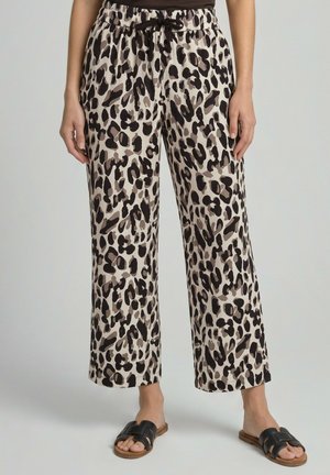 Losse beige broek met zwarte en bruine luipaardprint, elastische taille met zwart trekkoord, gedragen met zwarte platte sandalen met open teen.