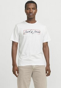 Hvid bomulds T-shirt med "Jack & Jones" logo i marineblå skrift med en rød rektangulær kant. Korte ærmer, afslappet pasform.
