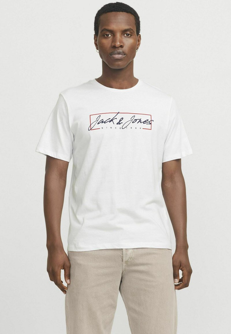 Hvid bomulds T-shirt med "Jack & Jones" logo i marineblå skrift med en rød rektangulær kant. Korte ærmer, afslappet pasform.