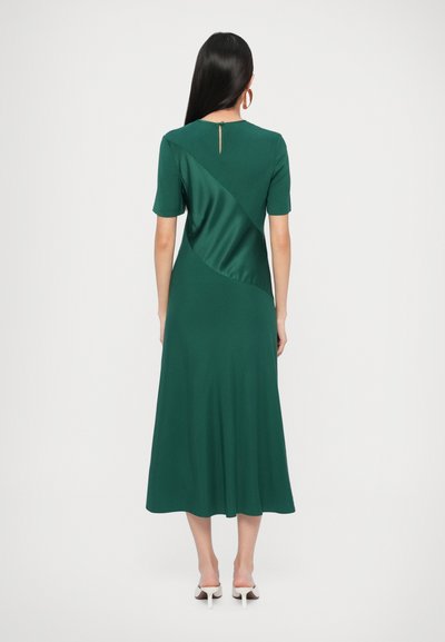Zelené midi šaty s krátkými rukávy, vybavené kontrastním saténovým panelem a výstřihem ve tvaru klíče na zádech. Hladká textura, splývavá silueta.