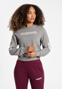 Grauer Hoodie mit weißem "HUMMEL"-Logo, gerippten Bündchen und kontrastierenden weißen Chevron-Details an den Ärmeln; kombiniert mit burgunderfarbenen Jogginghosen.