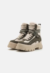 Kraftige high-top støvler i olivengrønt læder og beige kunstpels, med sorte mærkebånd og en tyk, struktureret gummisål.