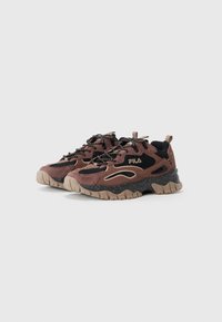 Zapatilla marrón y negra con materiales de ante y malla, que presenta una suela gruesa, acentos texturizados y cordones con patrones. Logo de la marca presente.