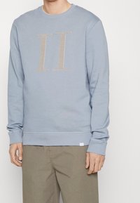 Felpa azzurra con scollo a girocollo, polsini e orlo a costine. Ricamo in beige con texture "II" sul davanti. Vestibilità casual.