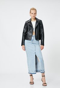 Svart skinn bältesjacka med dragkedjor, vit kort topp, höga ljusblå denimkjol med framtill slits, och svarta remmar med klackar.