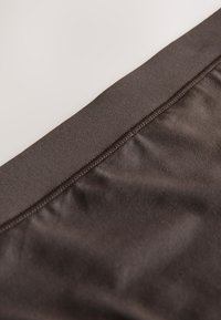 Primer plano de tela marrón oscura con textura suave y una costura cuidadosamente cosida a lo largo del borde.