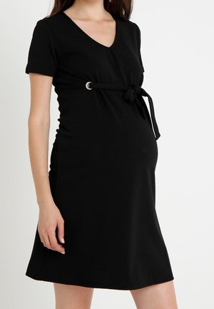 Donna incinta che indossa un abito premaman nero a maniche corte con scollatura a V e cintura annodata sopra la pancia.