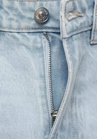 Jeans in denim azzurro chiaro con chiusura a bottone argentato, zip esposta e una consistenza sottile. Presentano tessuto sfrangiato vicino all'area della zip.
