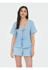 Top blu, strutturato, a maniche corte con scollatura profonda a V e fiocco frontale, abbinato a pantaloni corti coordinati, entrambi in un tessuto morbido e leggero.