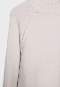 Lyserød strikket sweater med høj hals, der har en struktureret stofkvalitet og raglanærmer. Nærbillede af krave- og skulderdetaljer.