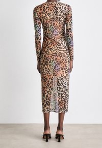 Robe en voile à manches longues avec un motif léopard dans des tons terreux et un effet dégradé, se terminant au milieu du mollet. Sandales à talons hauts noires.