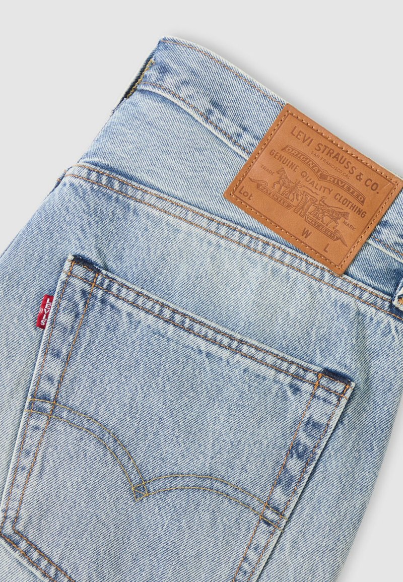 Jeans di denim azzurro chiaro con patch in pelle marrone che mostra il logo "Levi Strauss & Co.", cuciture dorate e un design distintivo della tasca posteriore.