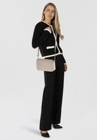 Bolso cruzado beige de forma rectangular, con textura suave y correa adjustable. Cárdigan negro con ribetes blancos y botones dorados.