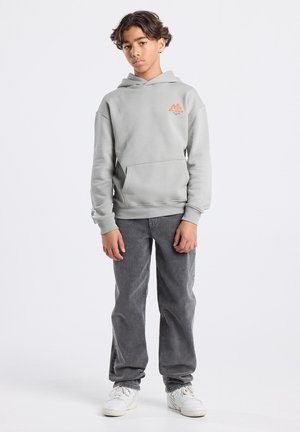 Hellgrauer Hoodie mit Kängurutasche und orangefarbenem Berg-Logo. Kombiniert mit dunkelgrauen weiten Jeans und weißen Turnschuhen.