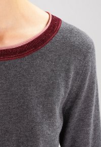 Pull gris avec un tissu texturé, un large col côtelé bordeaux et un corps lisse. Le mélange crée un look confortable.